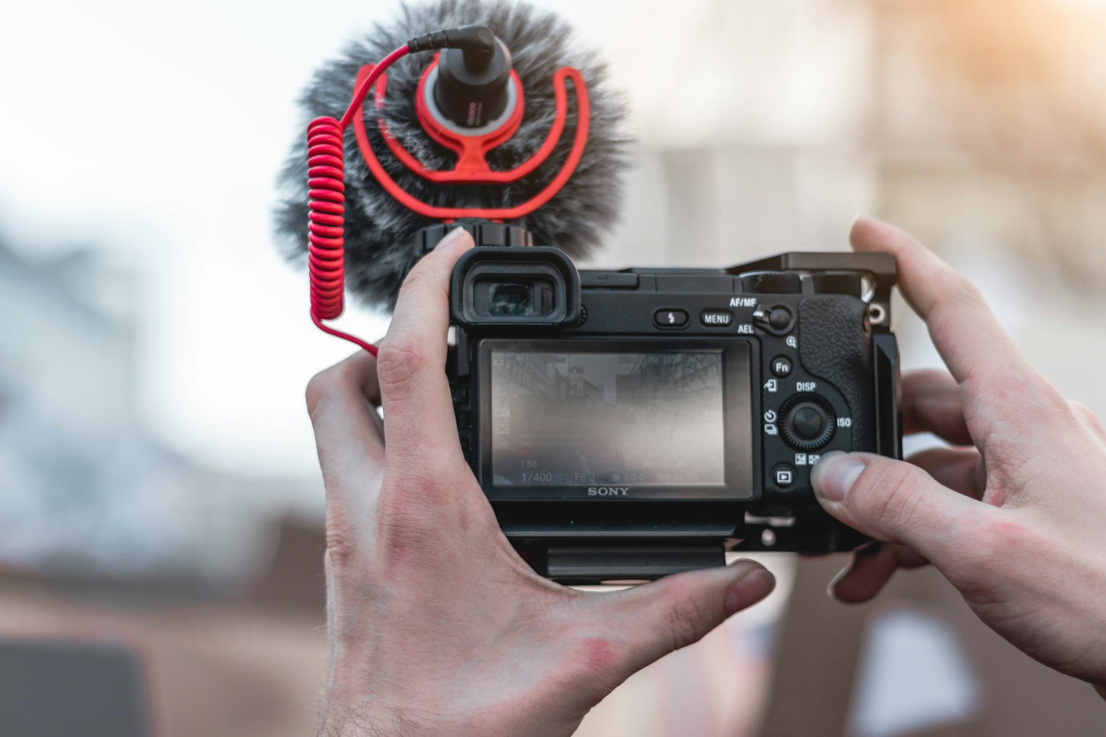 A content creator holding a vlogging camera and microphone from behind, representing the search for the right ElevenLabs voice