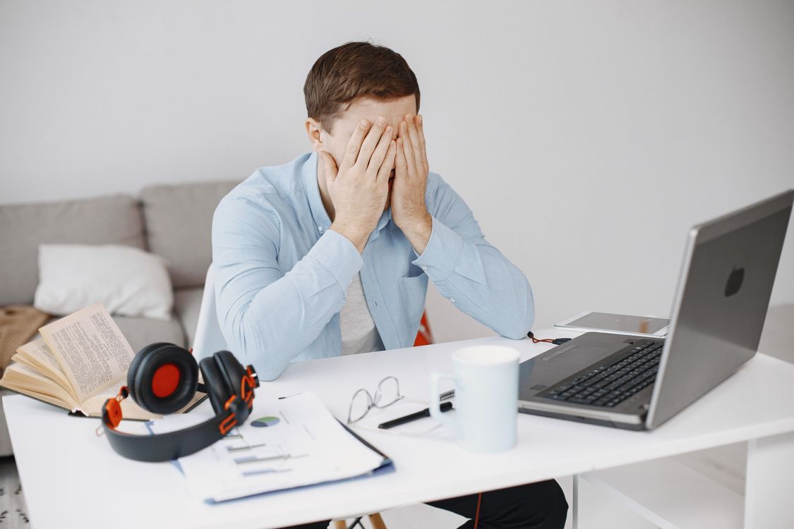 A frustrated professional holds his head while dealing with an AI presentation tool problem at his laptop