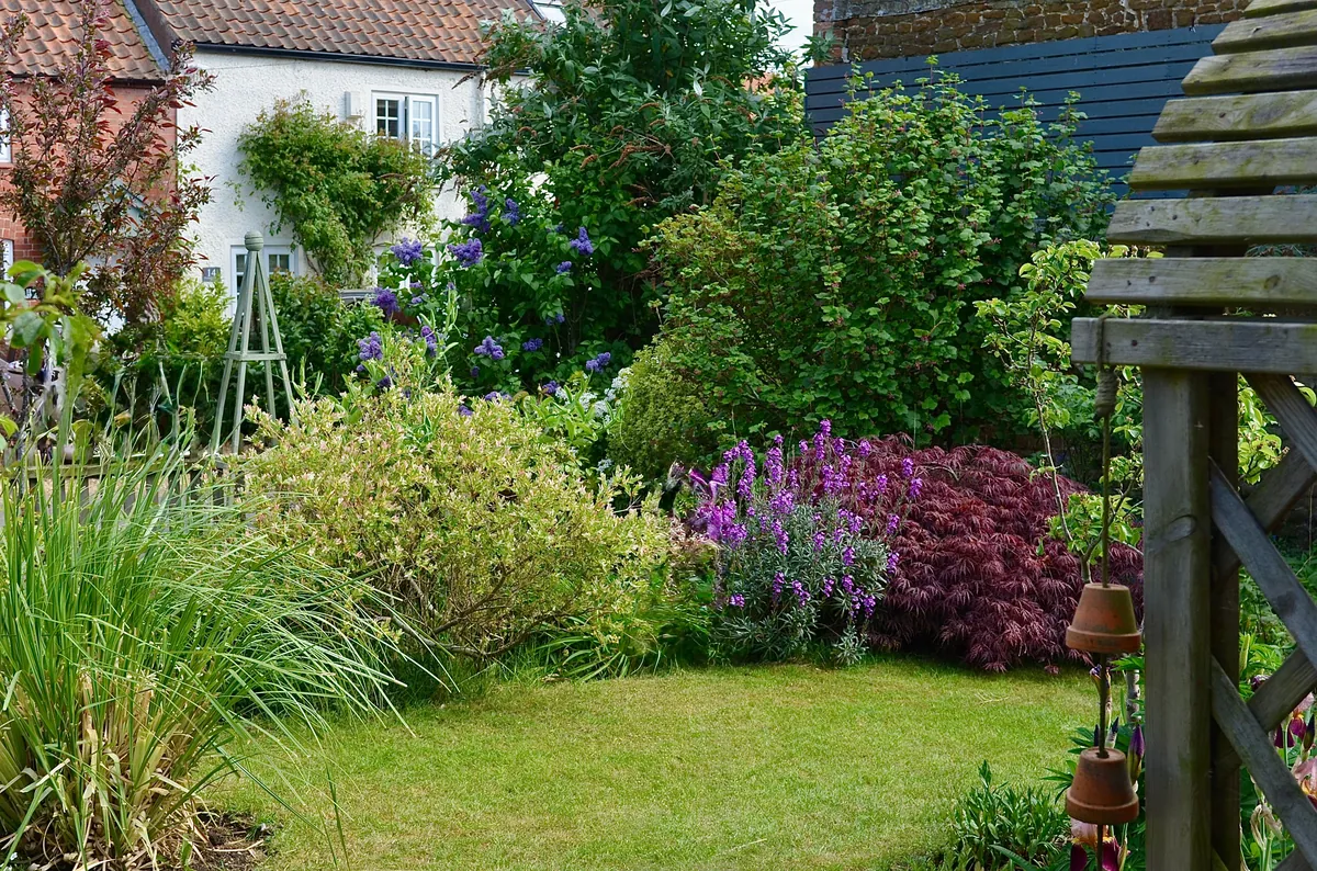 A lush English cottage garden in full bloom beside a rustic cottage