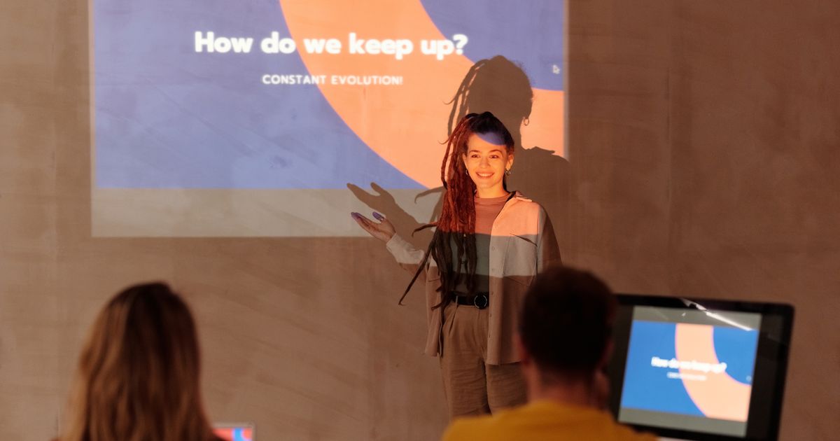 A presenter shows an exported slide deck on screen to an audience in a modern meeting room