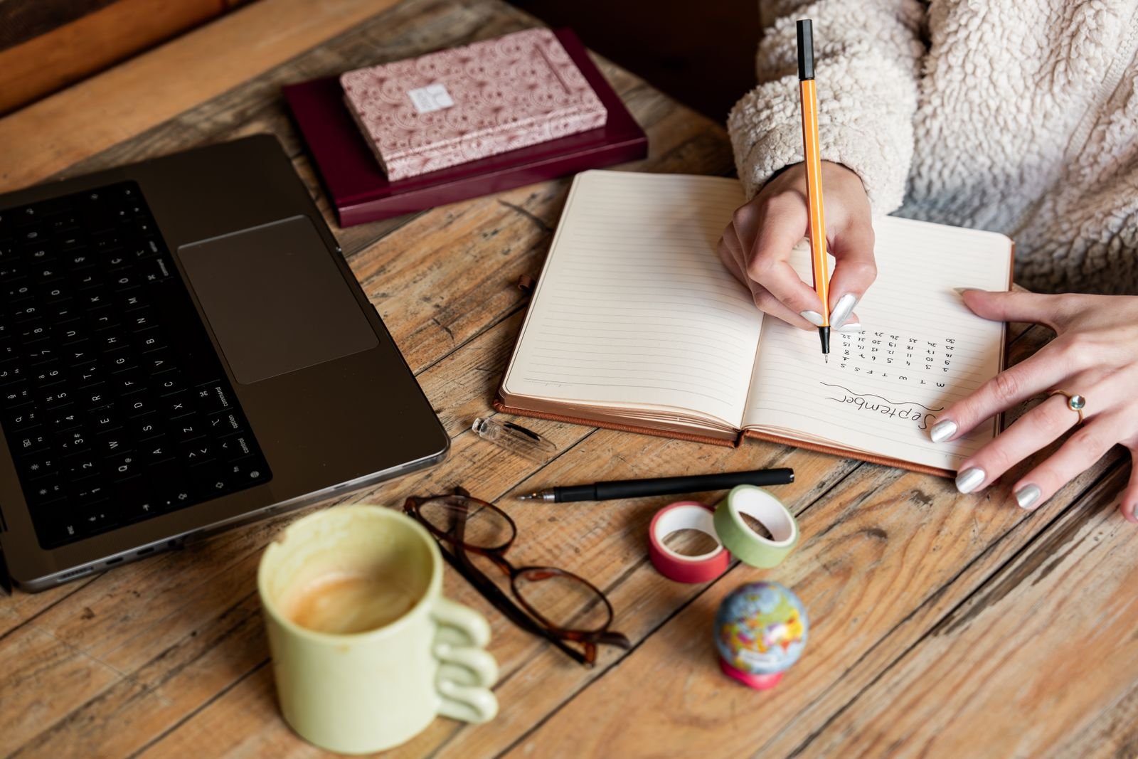 A person planning notes in a notebook beside a laptop and coffee