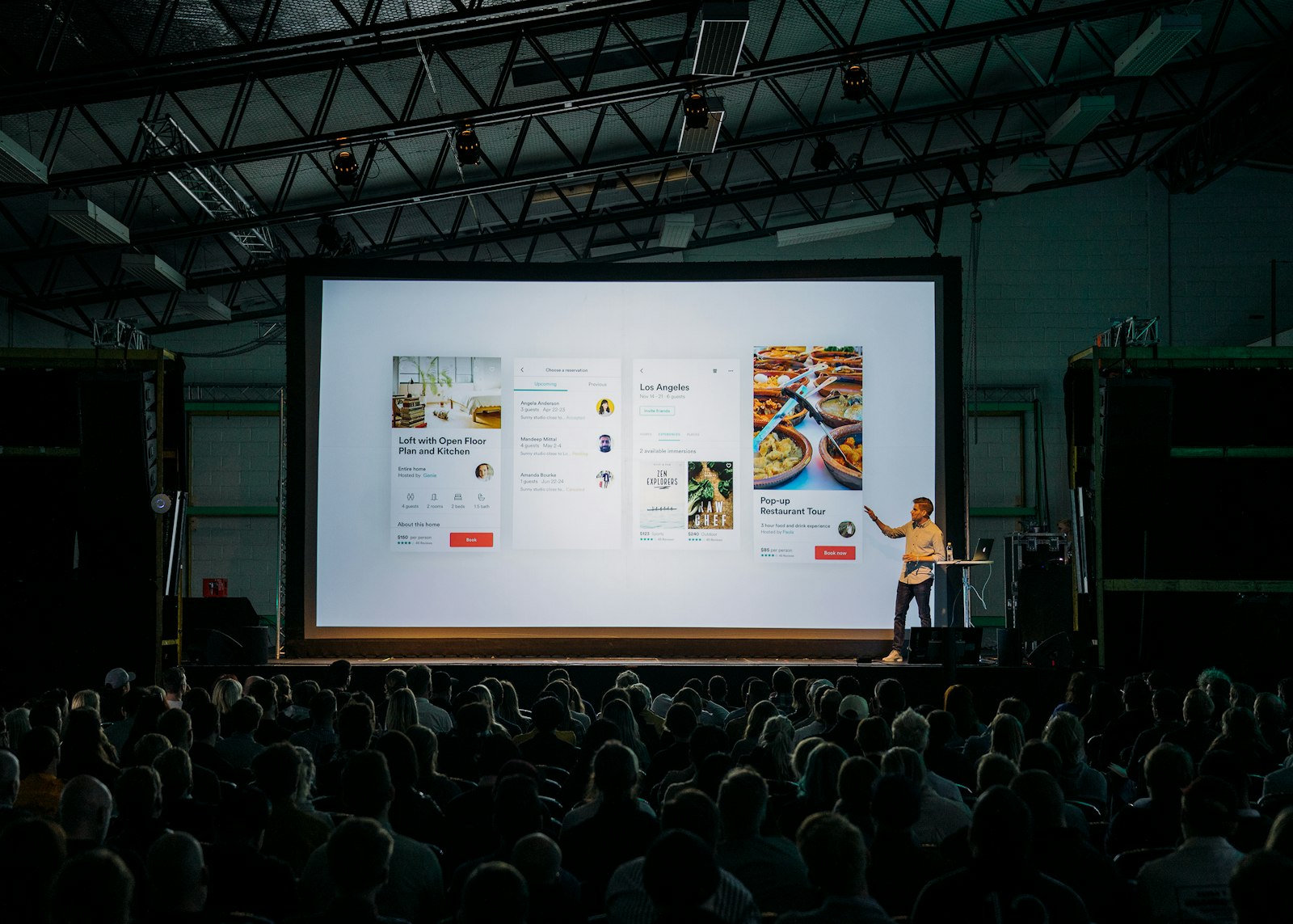 Person presenting slides on a large screen to an audience in a meeting room