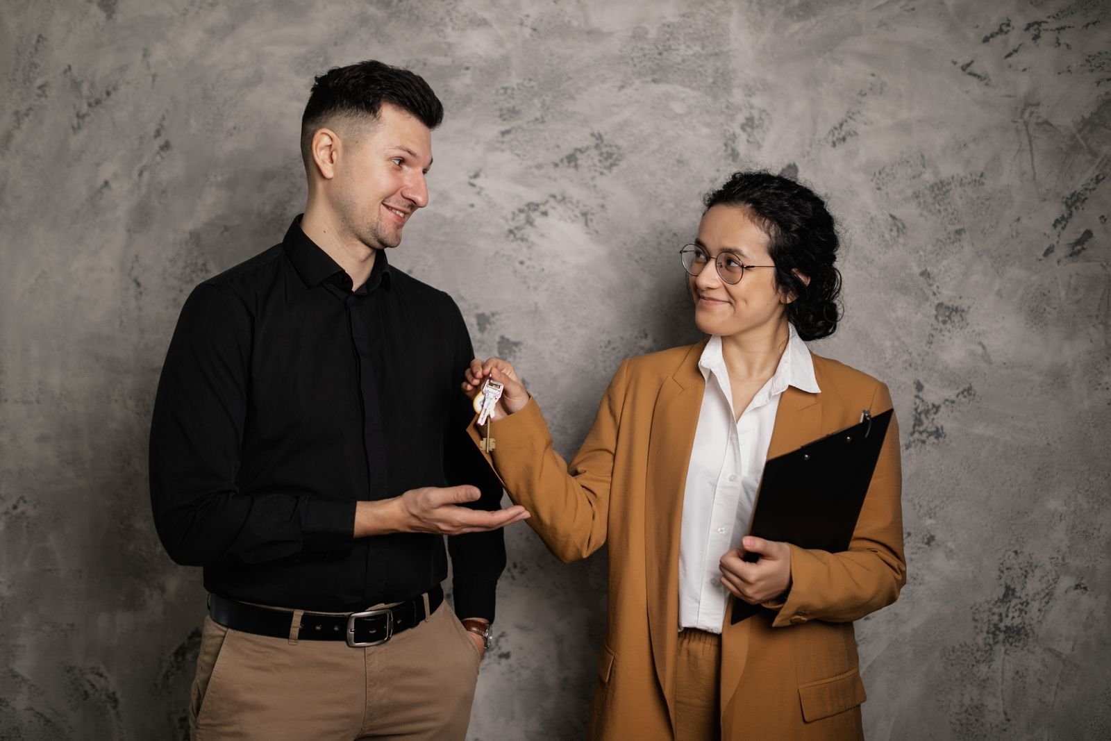 A real estate agent with a clipboard handing house keys to a client
