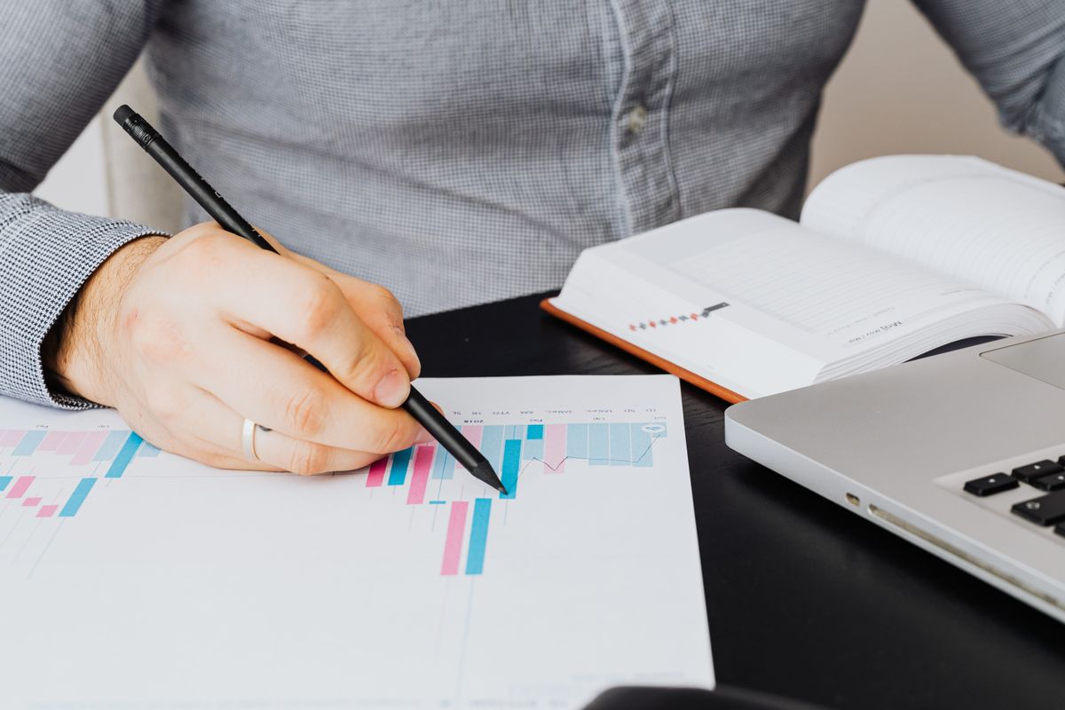 A person checking a summary on a laptop against a printed report