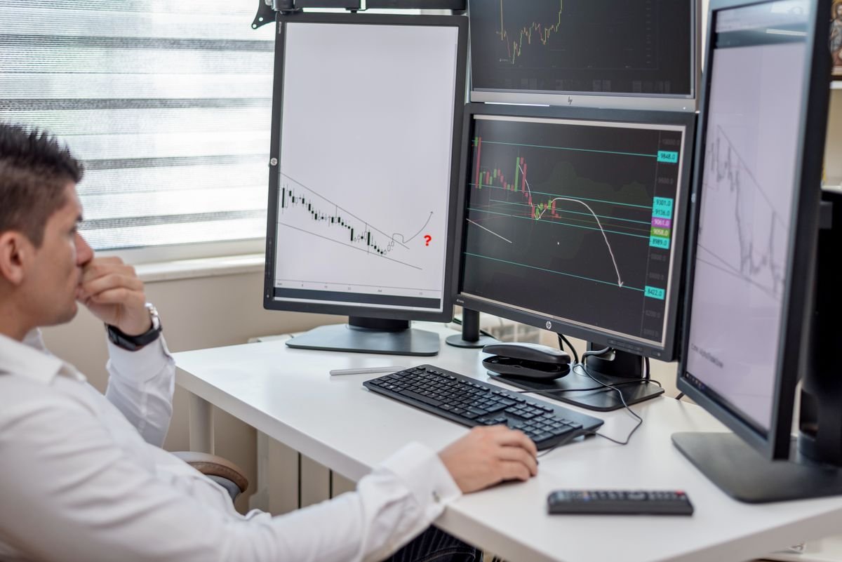 A professional evaluating data across multiple computer displays at a workspace