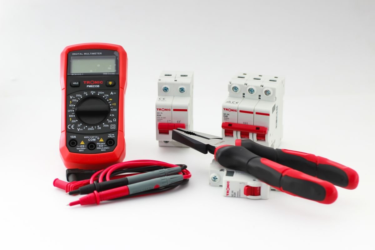 A digital multimeter and hand tools laid out beside circuit breakers for electrical testing