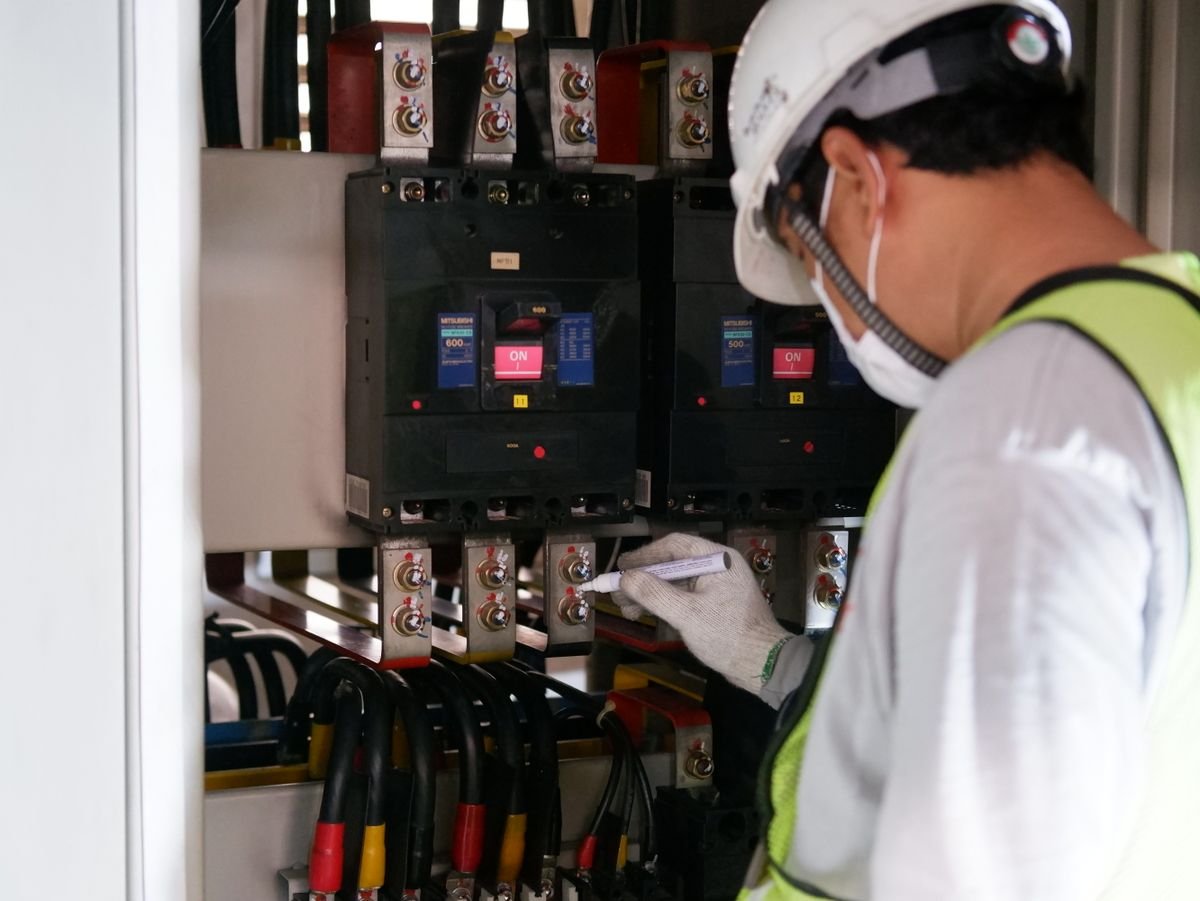 A technician checks voltage on an industrial electrical panel full of breakers