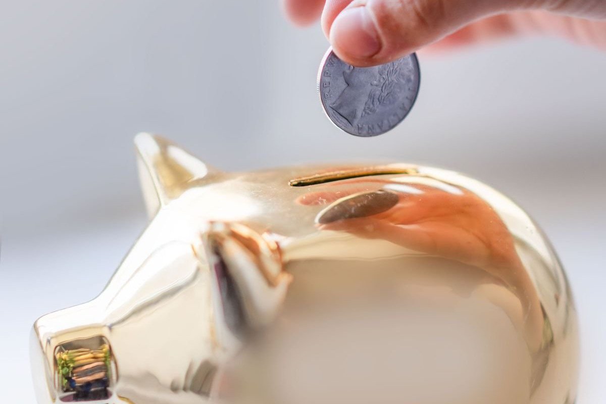 A hand dropping a coin into a golden piggy bank, representing budgeting for AI research tool subscriptions
