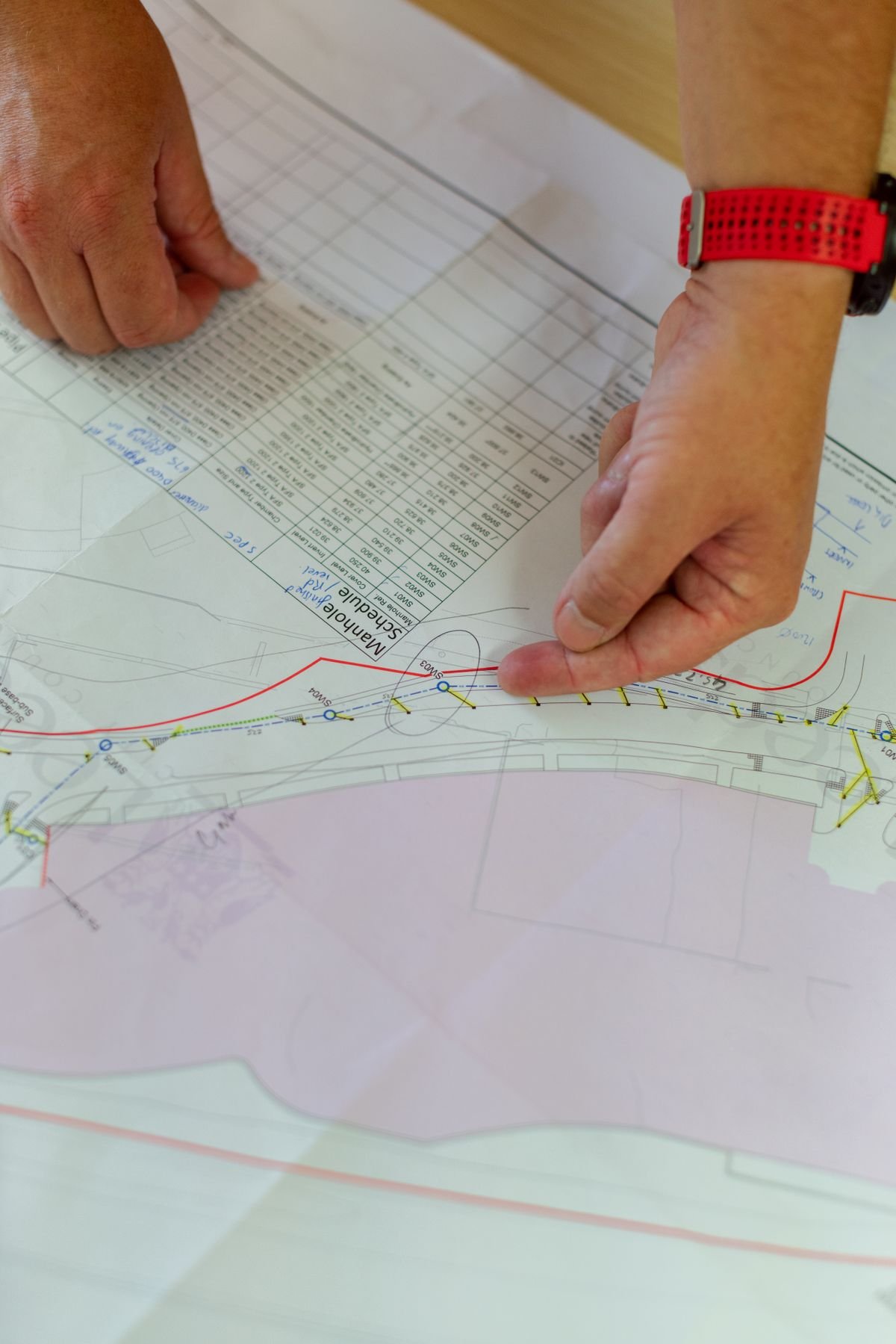 Engineer's hands pointing at a marked-up structural drawing with a level schedule table