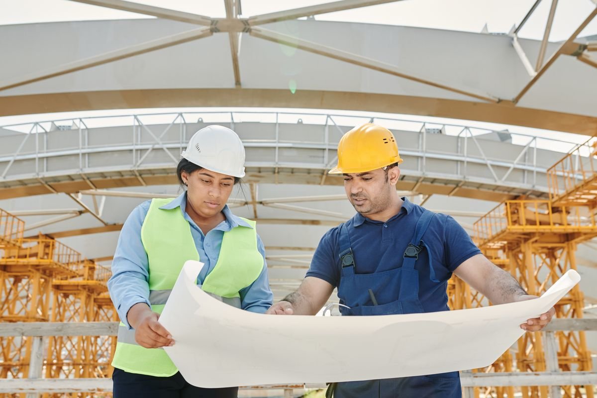 Two structural engineers in hard hats reviewing a large blueprint on a steel-framed construction site