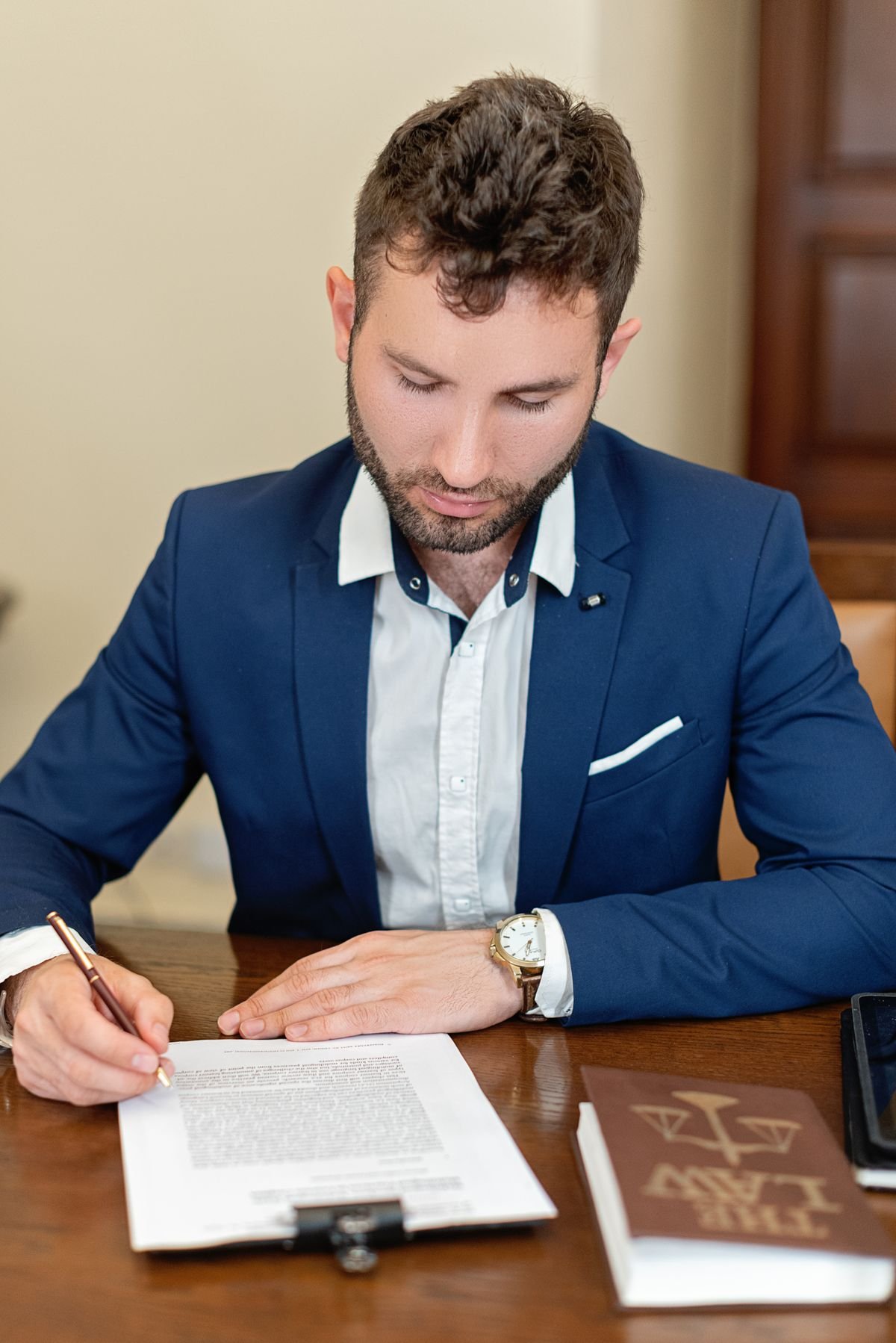 A professional in a suit reviewing and signing a legal document at a desk beside a law reference book