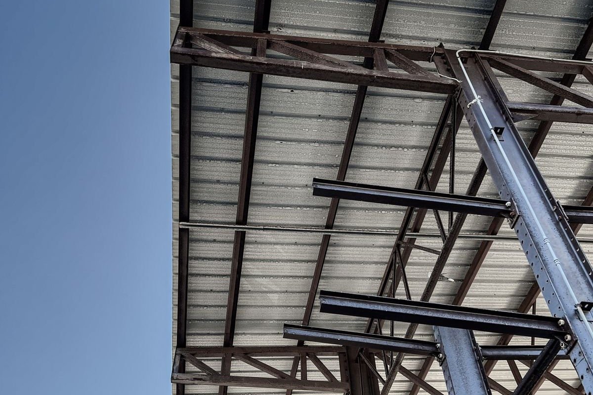 Upward view of a steel roof structure with beams and trusses against a blue sky