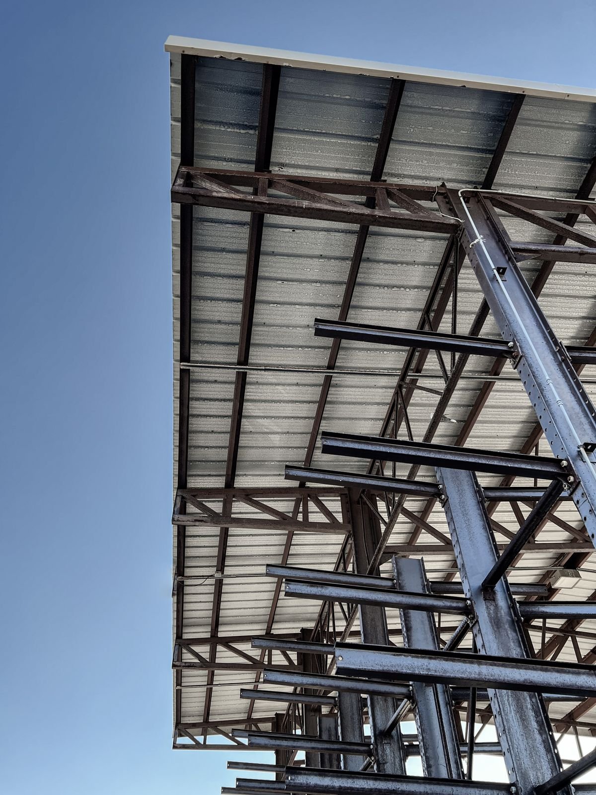 Upward view of a steel roof structure with beams and trusses against a blue sky