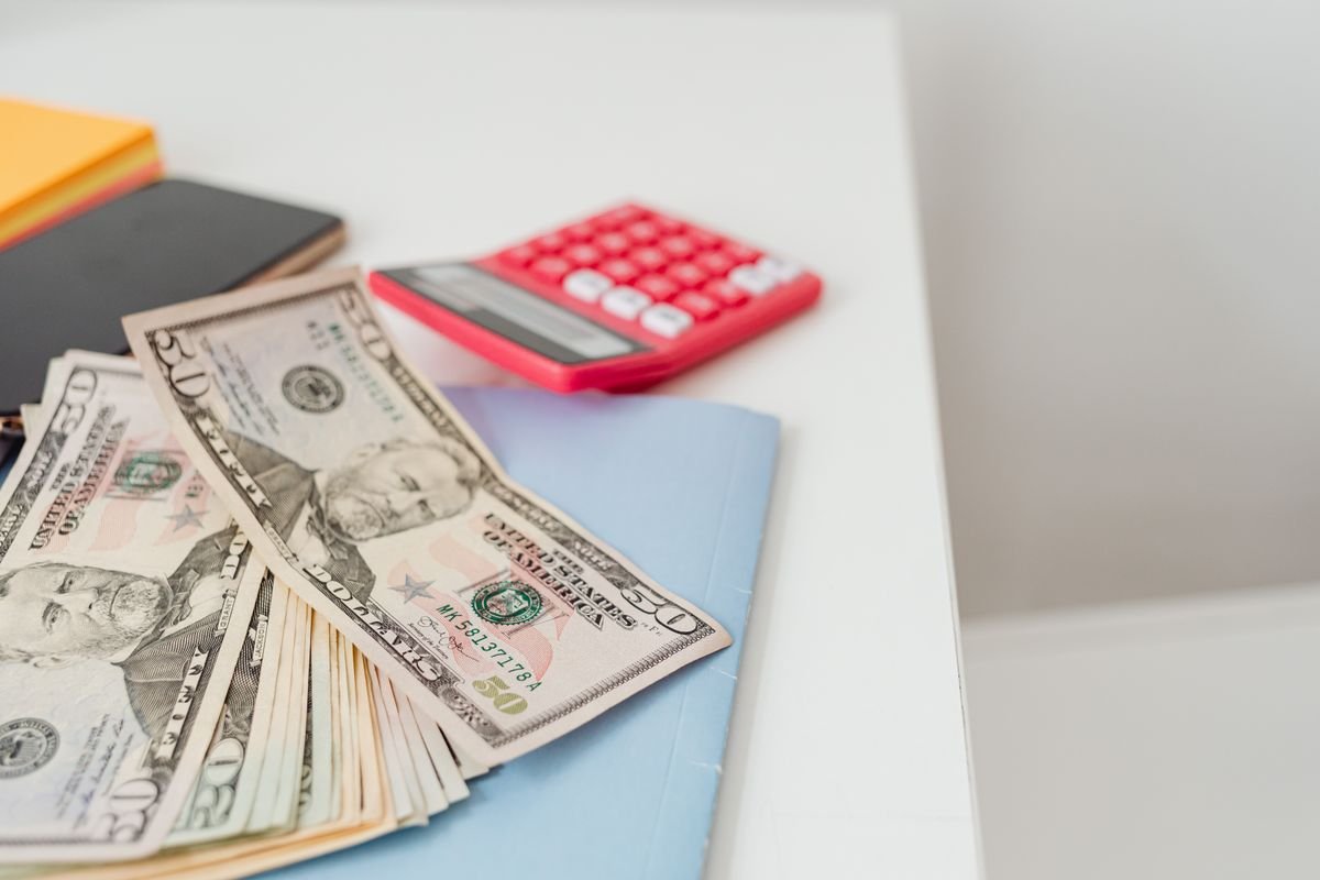 US dollar bills beside a red calculator and notebooks on a desk, representing AI tool pricing compared side by side