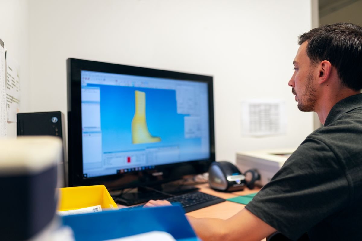 Engineer at a desk viewing a 3D CAD model on a computer monitor