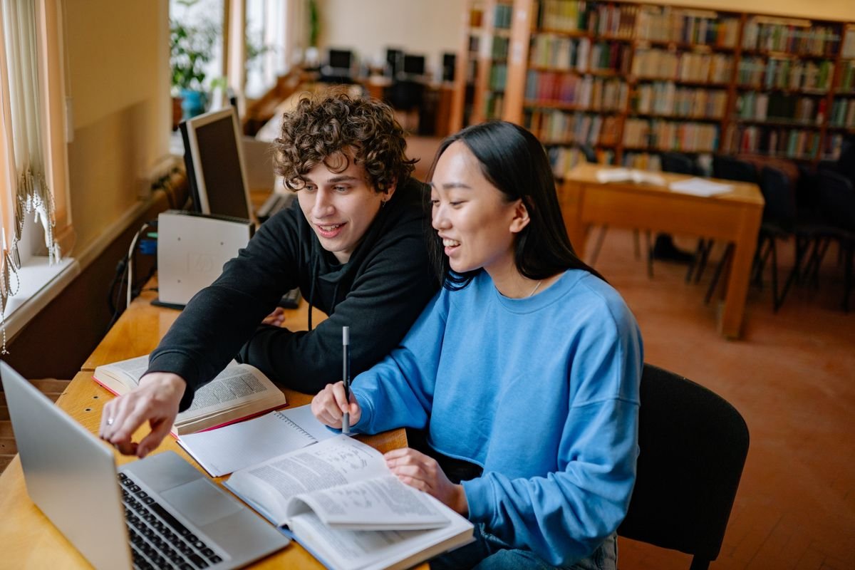 Two students comparing research tools on a laptop in a university library