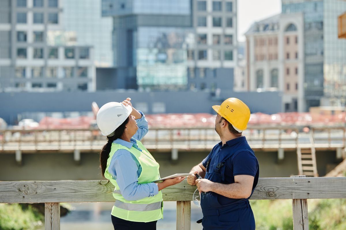 Two civil engineers reviewing construction plans on a site with a city skyline behind them