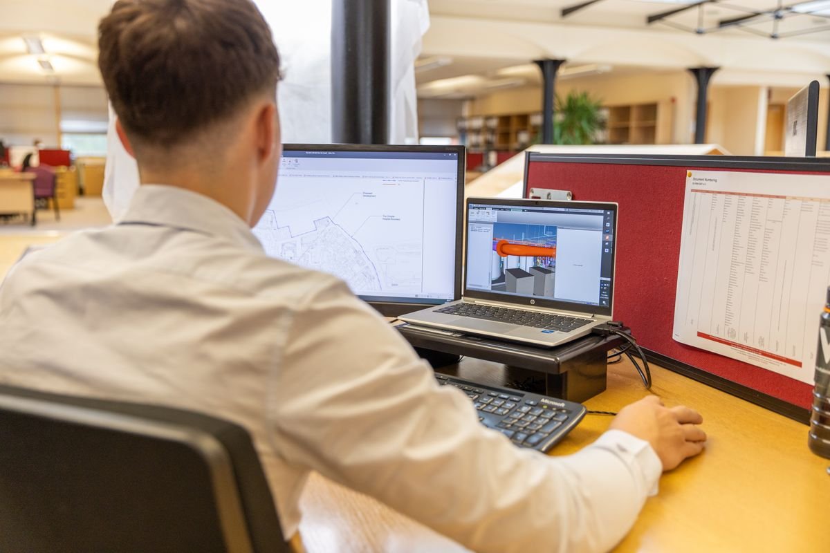 An engineer working on a CAD design at dual monitors in a bright office