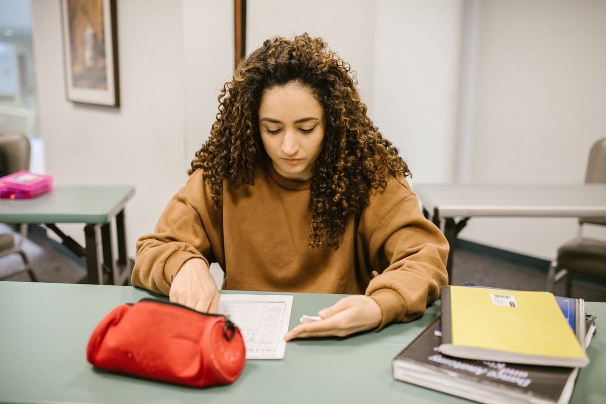 Student revising for an exam surrounded by books and notes in a classroom