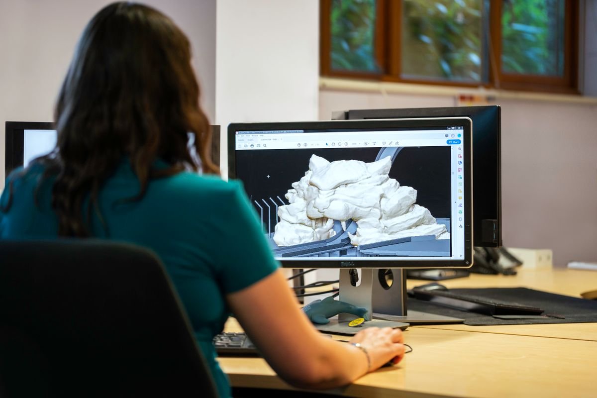 A person viewing a 3D model on a desktop monitor in CAD modeling software