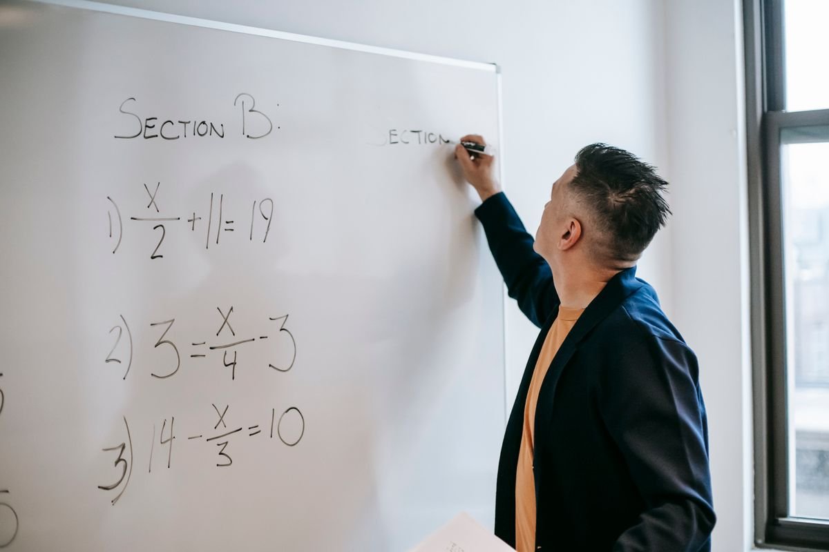 Engineer working through algebra equations by hand on a whiteboard