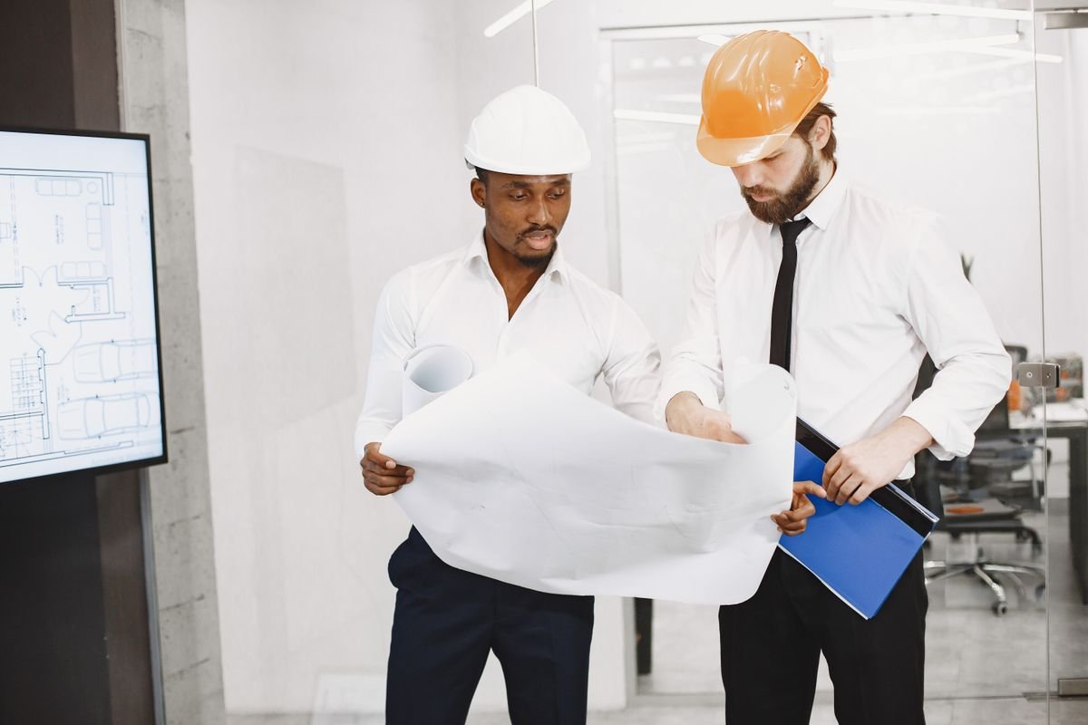 Two architects in hard hats reviewing a blueprint together in an office