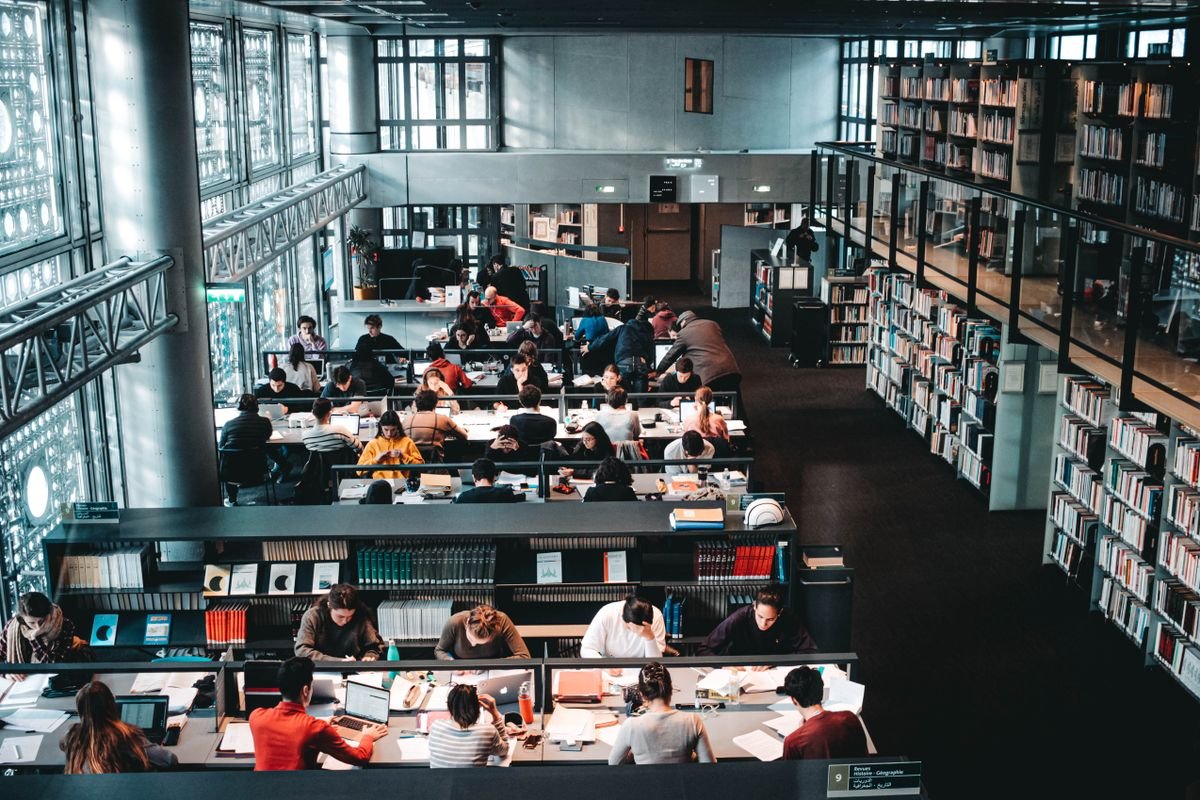 Students with laptops and books researching together in a public library