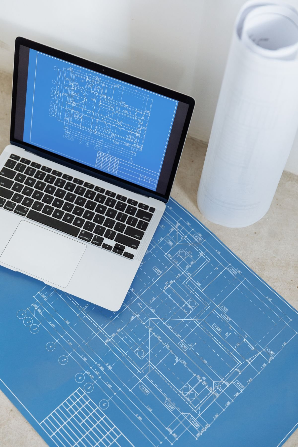 Laptop showing an engineering blueprint beside rolled drawings on a table