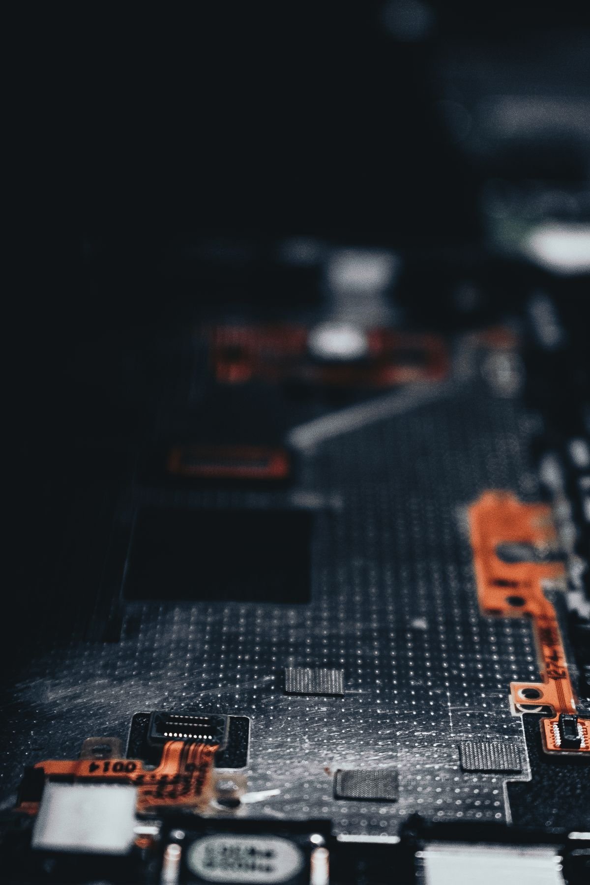 Dark close-up of a circuit board with orange flex connectors and surface-mount components