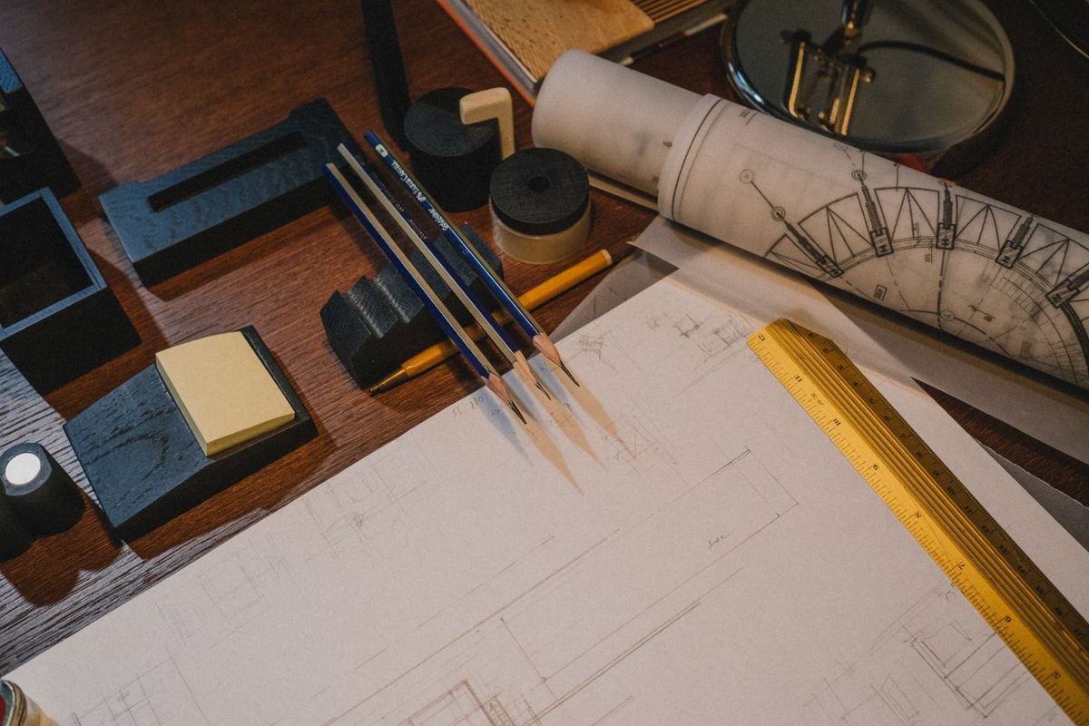 Overhead view of blueprints, sketches, and drafting tools on a wooden desk