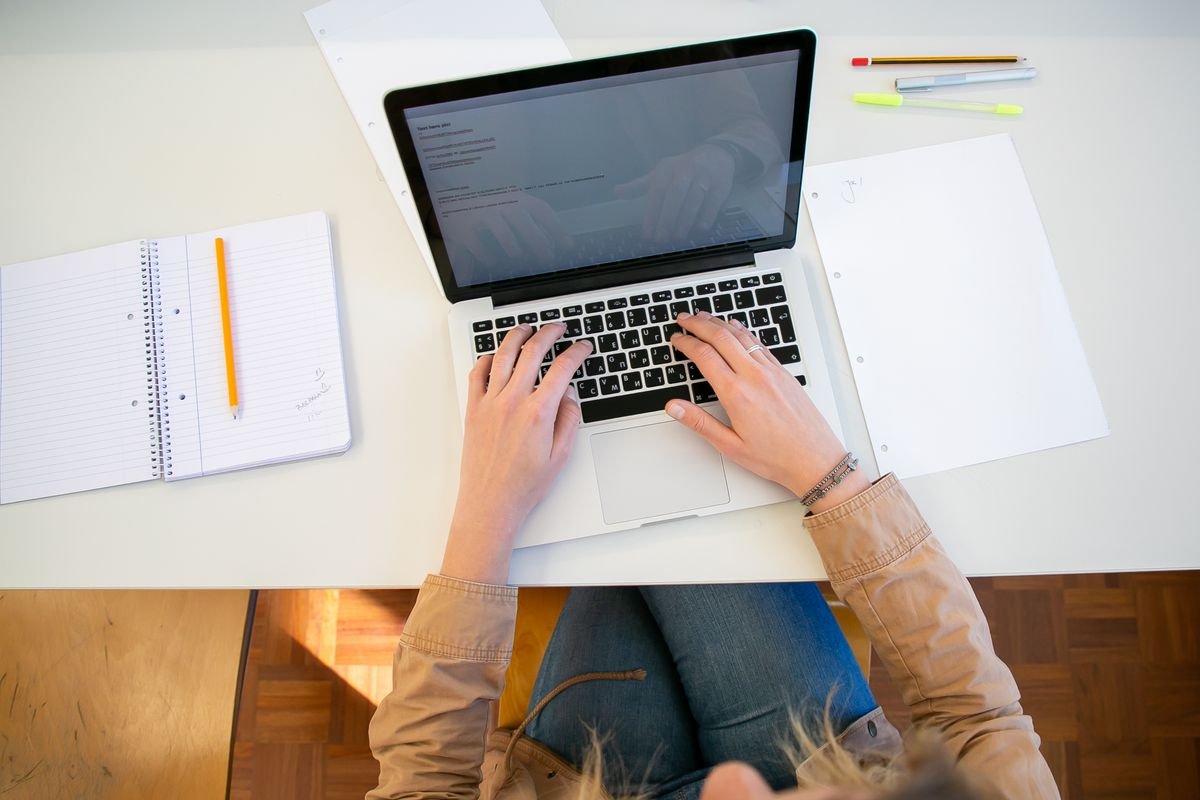 Overhead view of hands typing on a laptop surrounded by notebooks and report documents