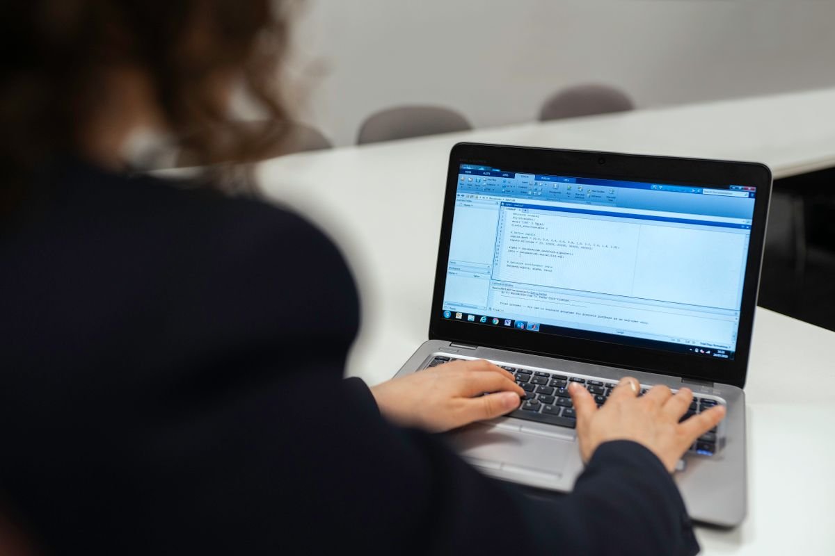 Engineering student focused on writing code at a laptop in a modern workspace