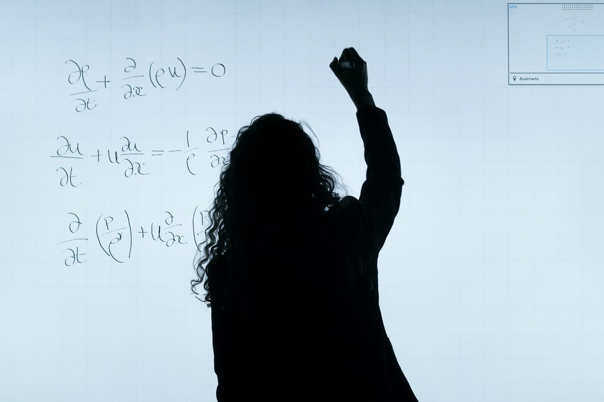 An engineer writing fluid-dynamics equations on a transparent glass board