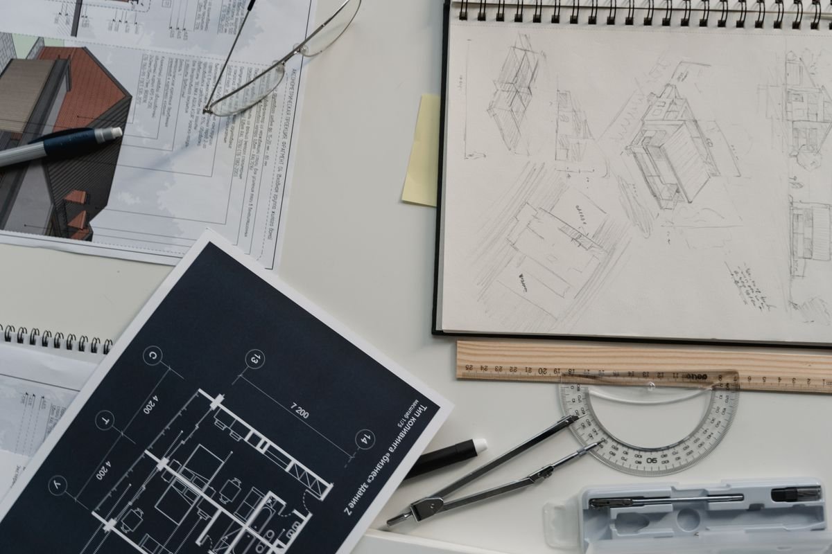Technical blueprints, an architectural sketch, and drafting tools laid out on a design desk