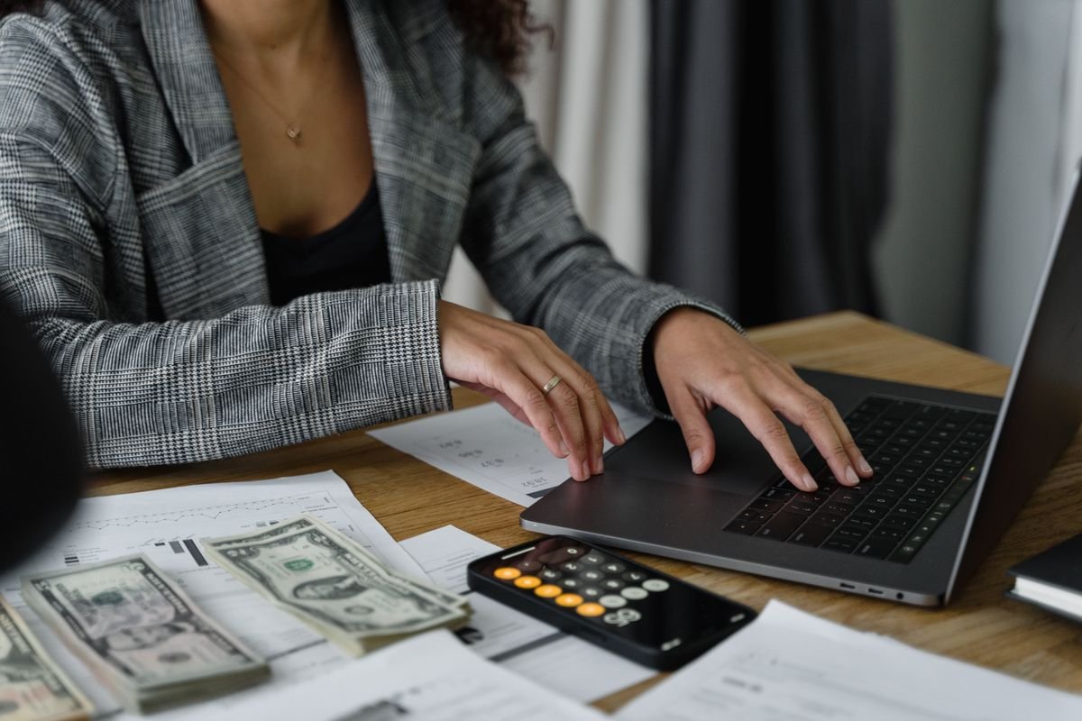 A professional reviewing costs on a laptop with cash and a calculator on the desk