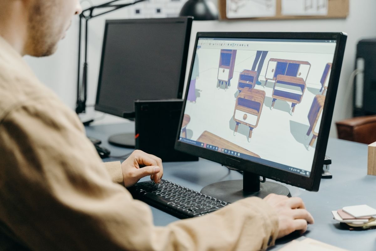 A designer working on 3D furniture models in CAD software on a desktop monitor