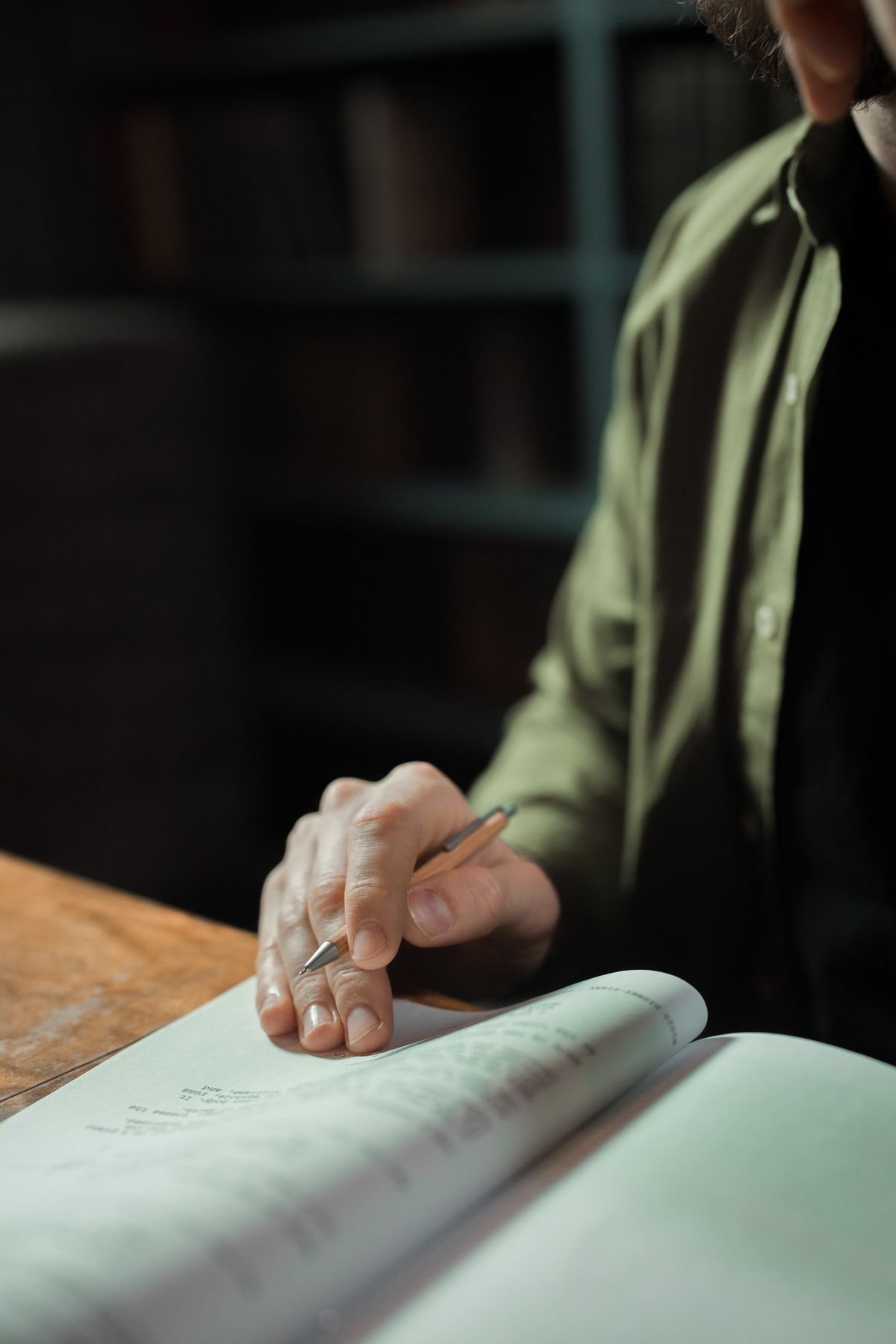 A person writing notes in a notebook in front of library bookshelves