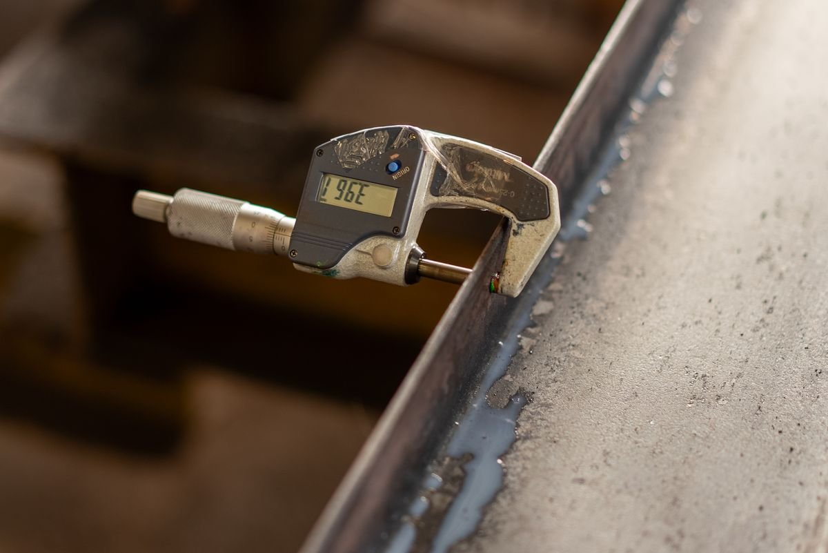 A digital caliper measuring the thickness of a machined metal object