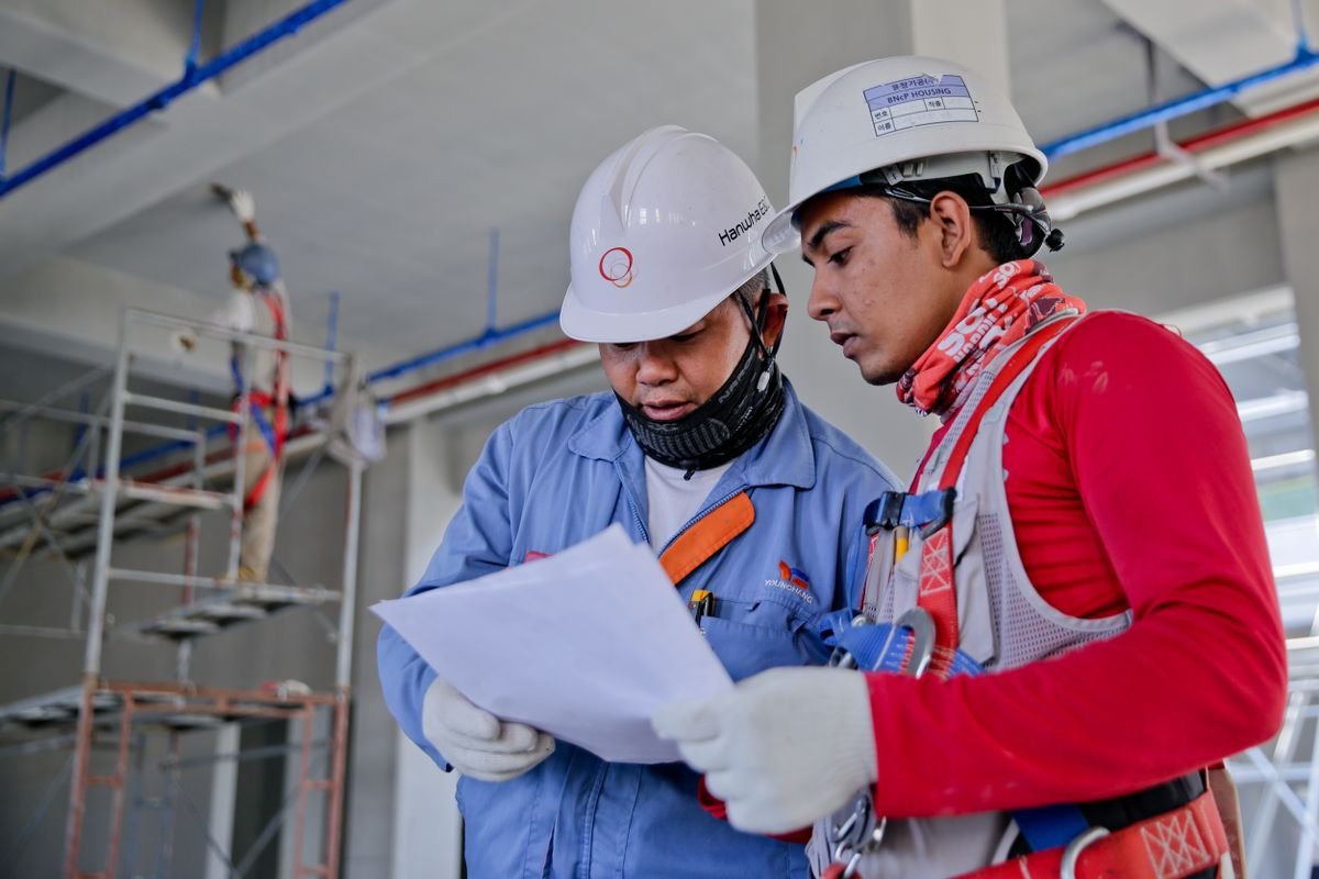 Two construction workers in hard hats reviewing a document together on site